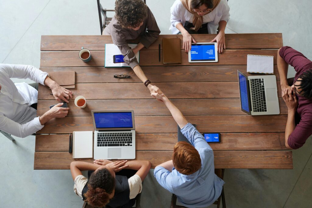 6 personnes autour d'une table, avec portable et 2 se donnent la main